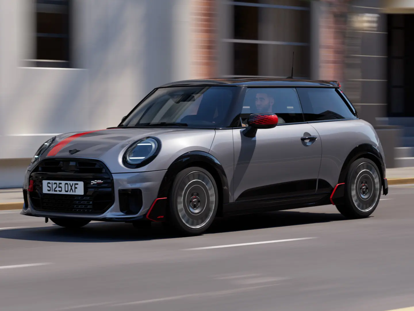 MINI Cooper 3-door in Melting Silver with John Cooper Works mirror cap and bonnet decal in Chili Red, roof spoiler and winglet in Black, driving along city street – front-side view.